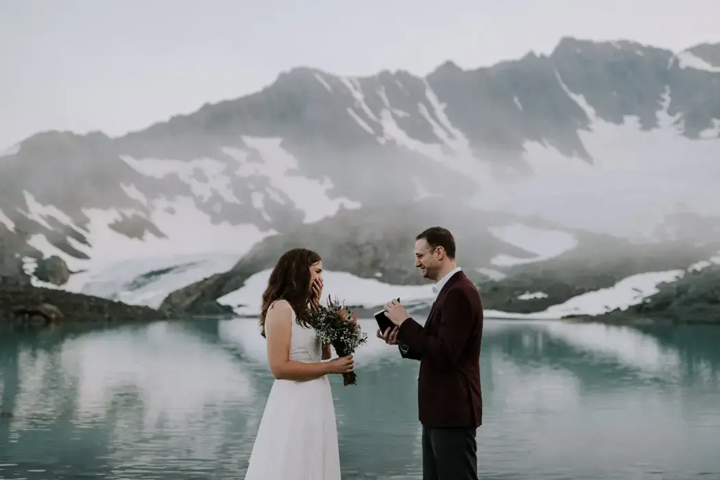 groom showing bride vows with mountain and lake backdrop