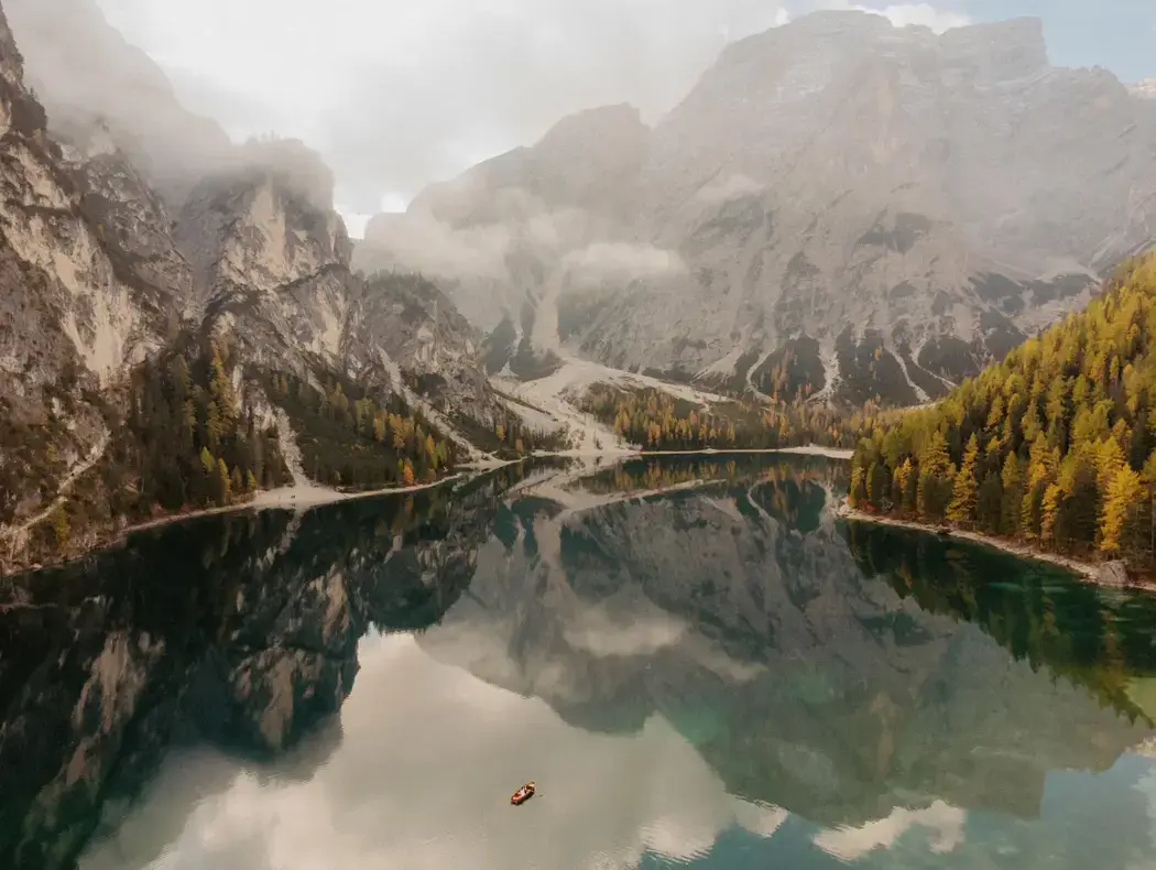 wide shot of tiny row boat on clear lake surrounded by mountains