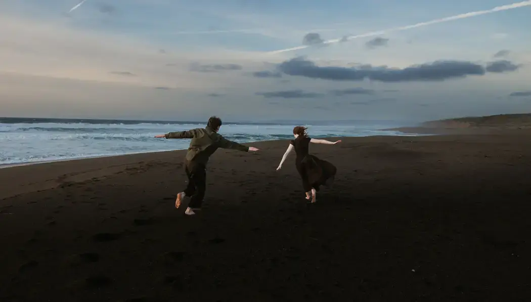 couple playfully running on black sand beach